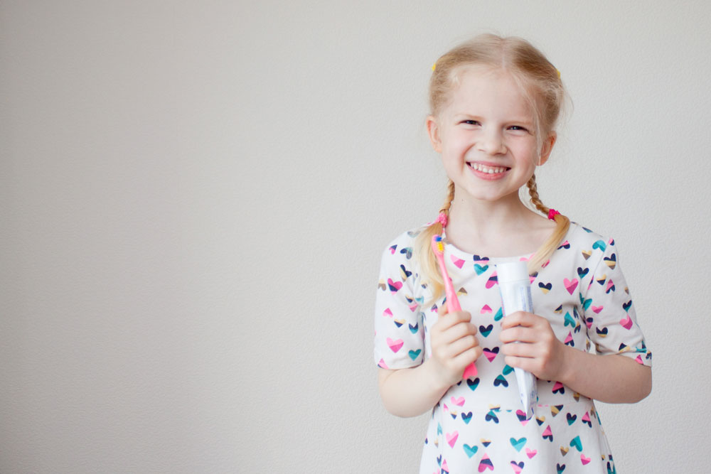 Child holding toothbrush and toothpaste after routine dental cleaning exam